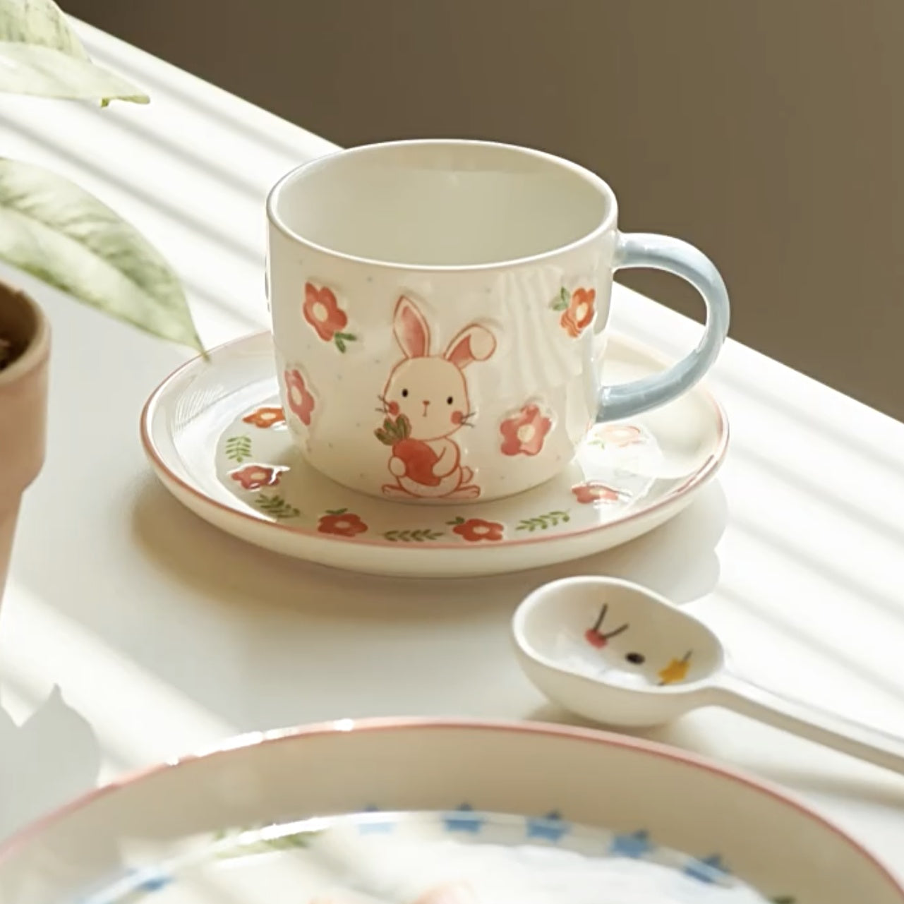 Ceramic cup with rabbit design on a saucer and spoon on a white surface