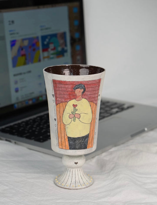 Man portrait pedestal ceramic cup displayed beside a laptop.