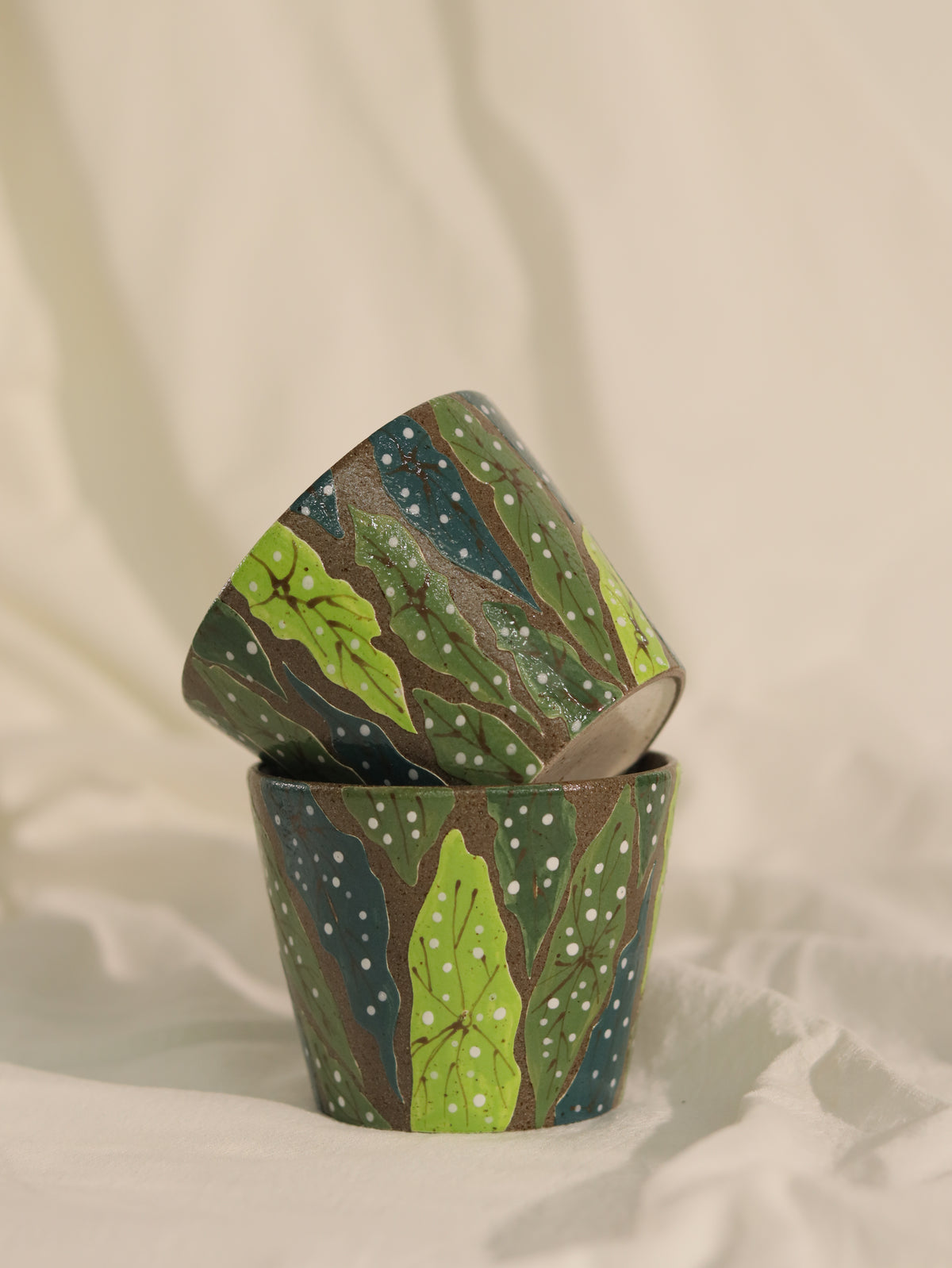 Two handcrafted forest leaf ceramic cups arranged on soft fabric.