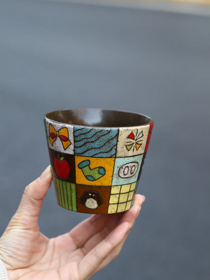 Ceramic cup with colorful patterns held by a hand against a gray background