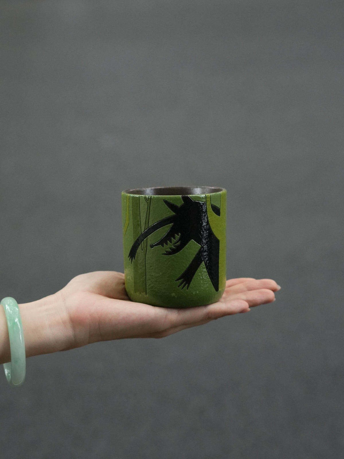 Hand holding a forest-green ceramic cup featuring the black silhouette of the Big Bad Wolf.