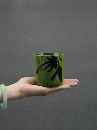 Hand holding a forest-green ceramic cup featuring the black silhouette of the Big Bad Wolf.