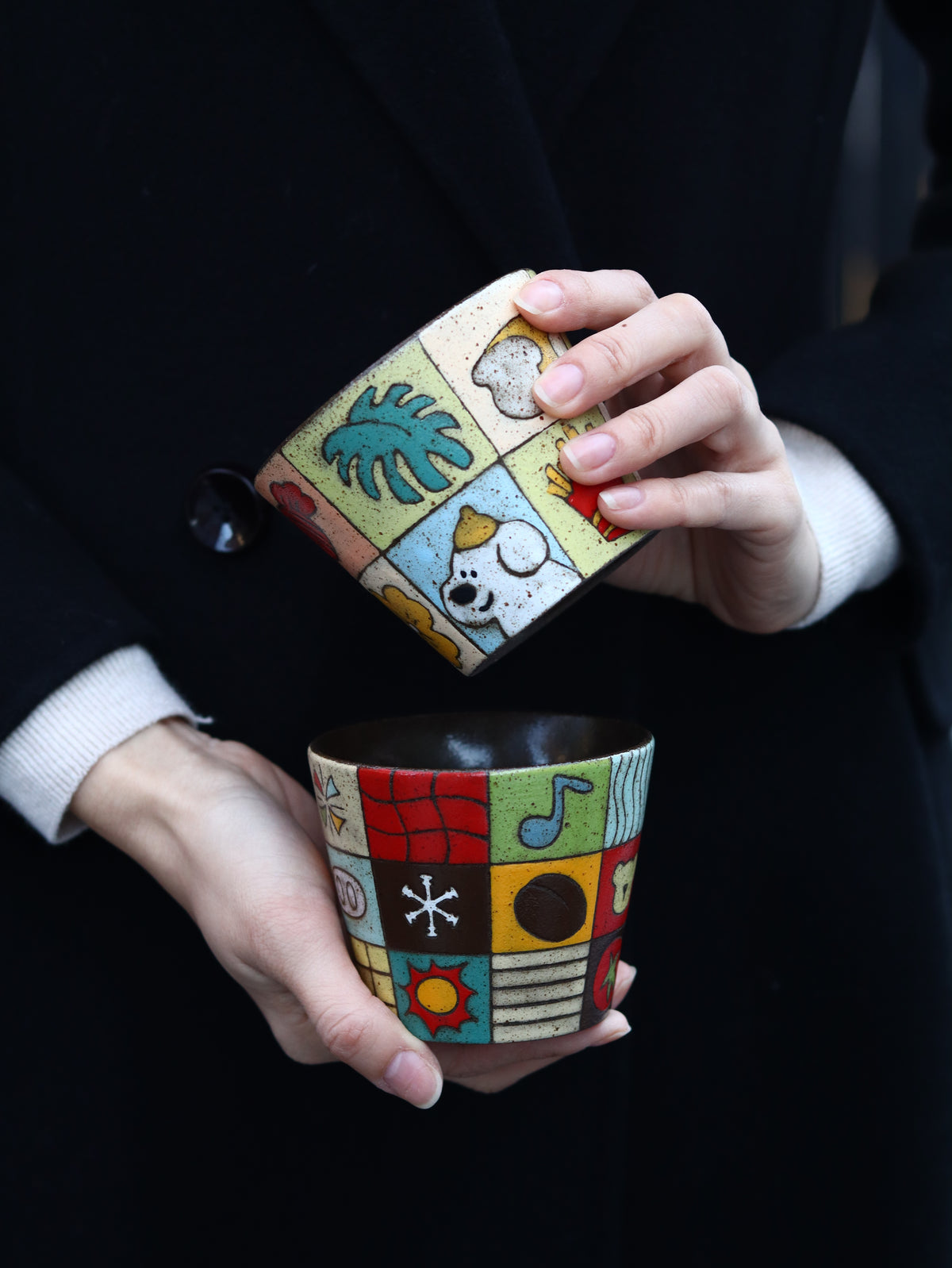 Two garden patchwork ceramic cups held together against a dark background.