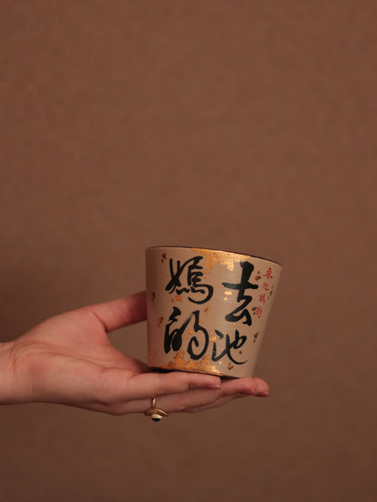 Hand holding a 260ml Chinese calligraphy ceramic cup with black brushwork, red details and delicate gold flecks.