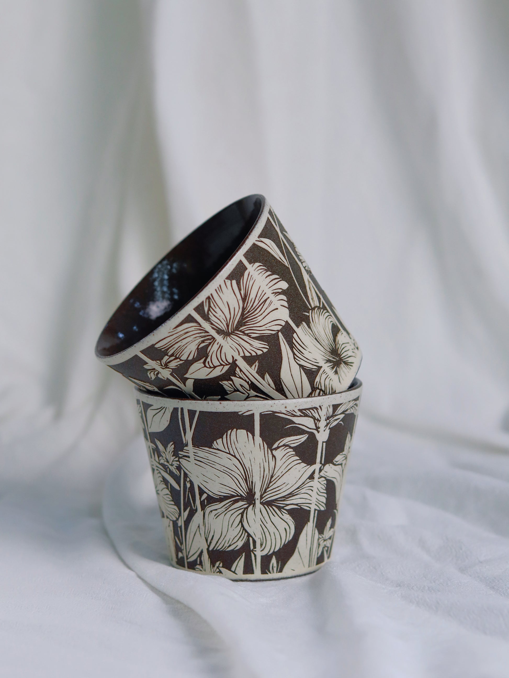 Two stacked handcrafted ceramic cups with carved floral patterns