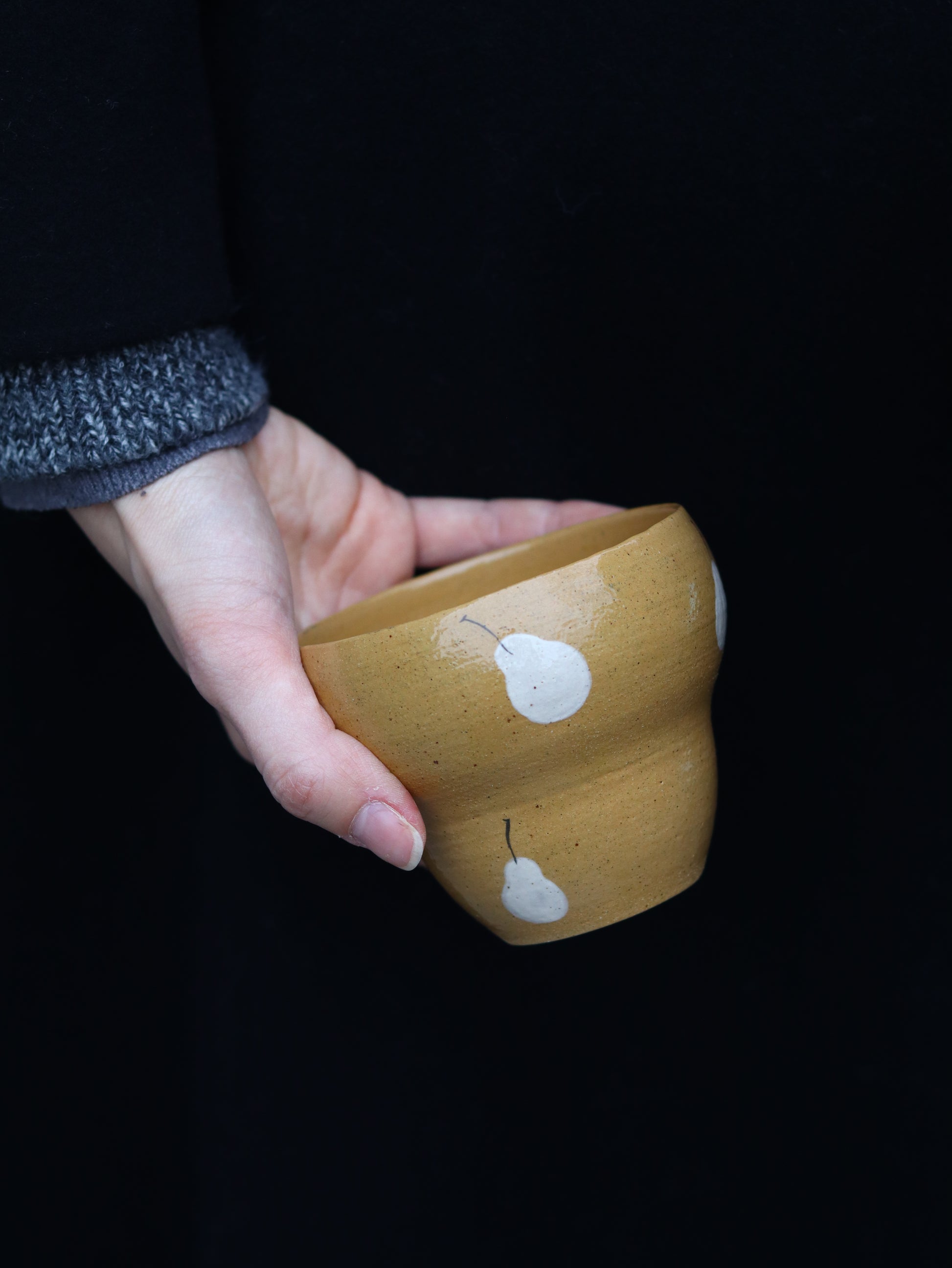 Hand holding a brown ceramic object with white floral designs against a black background