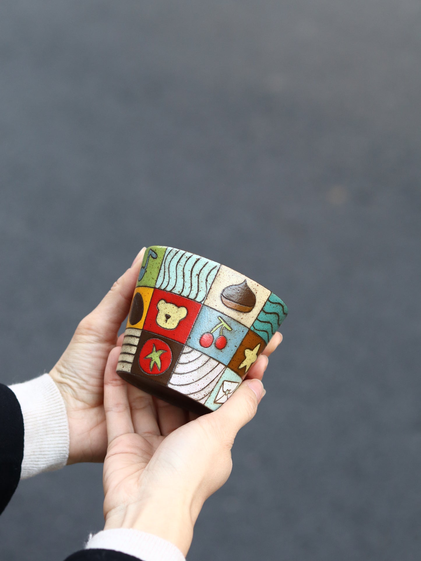 Hand holding a small, colorful wooden box with geometric patterns against a dark background