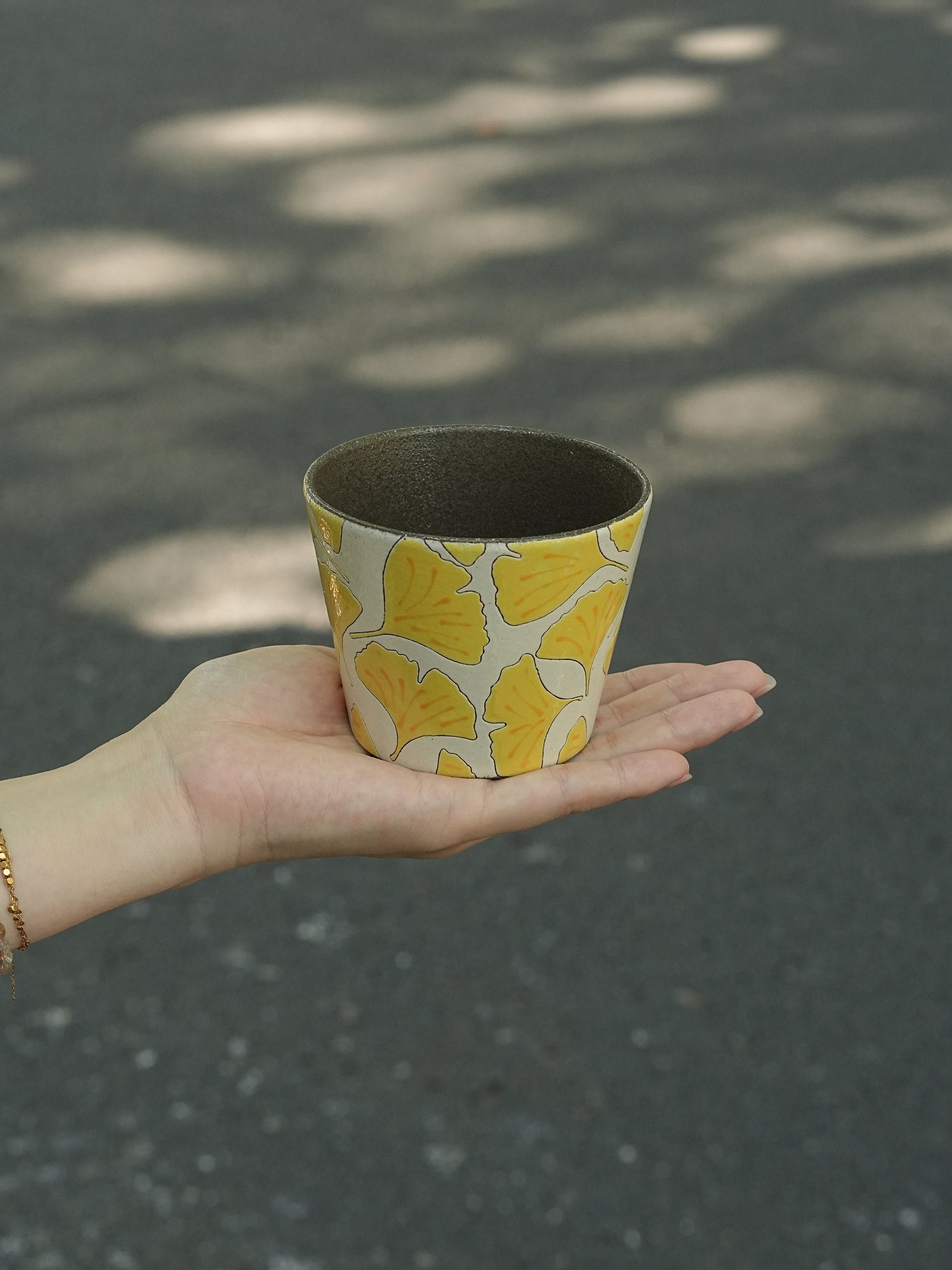 Hand holding a 270ml hand-painted ginkgo ceramic cup with carved yellow leaf outlines
