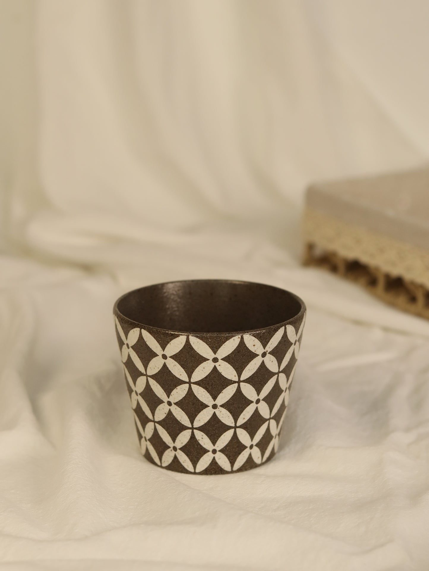 Decorative pot with geometric pattern on a white fabric background
