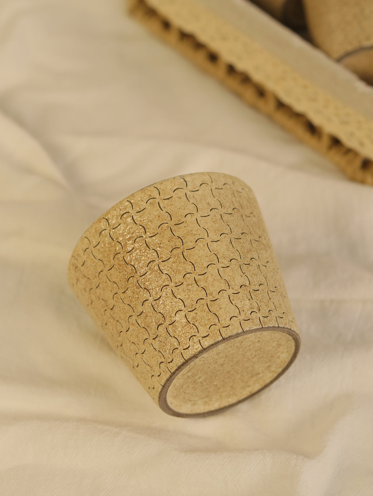 beige ceramic cup resting on soft fabric, showing its carved geometric texture.