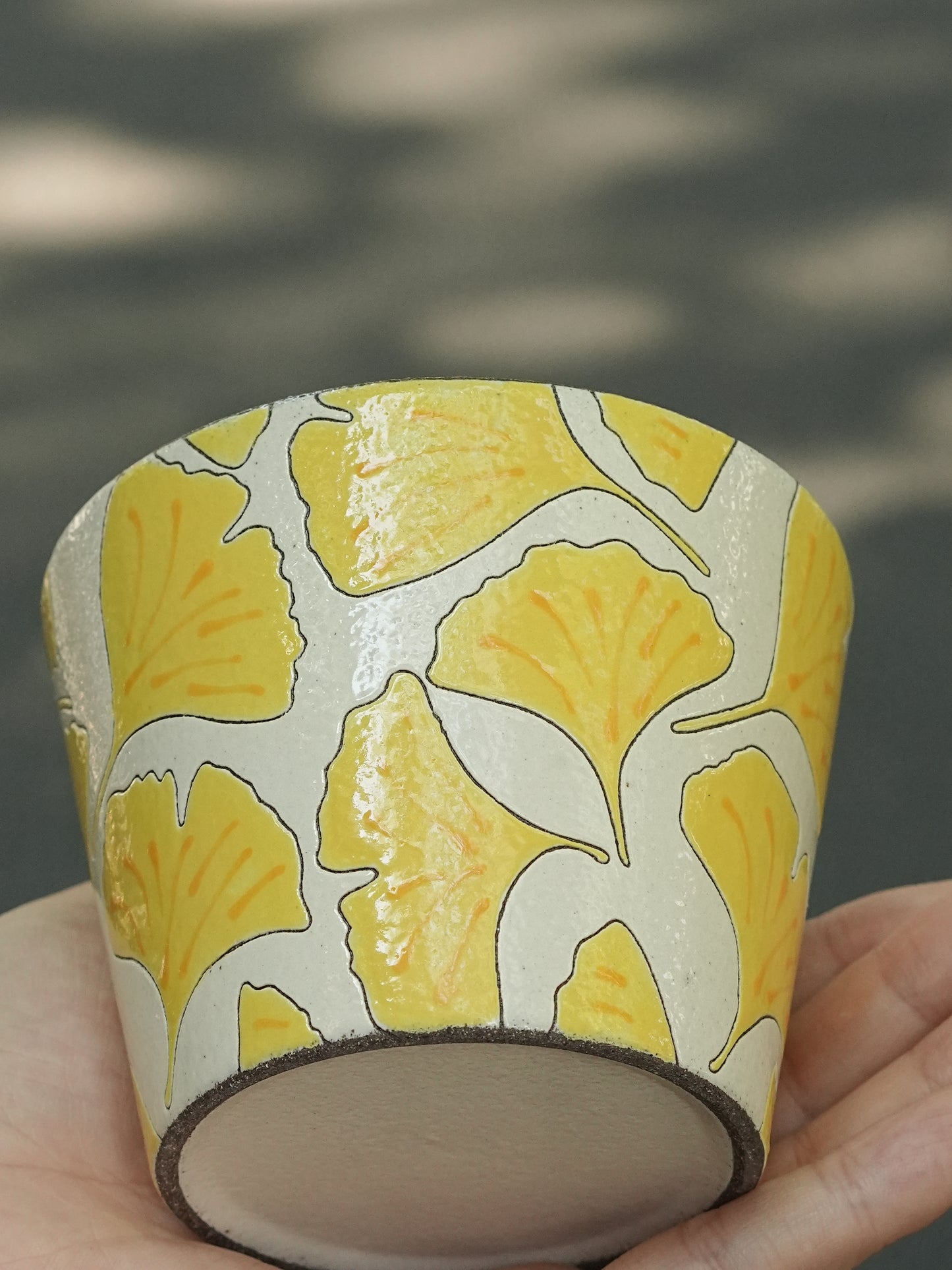 Hand holding a 270ml hand-painted ginkgo ceramic cup with carved yellow leaf outlines