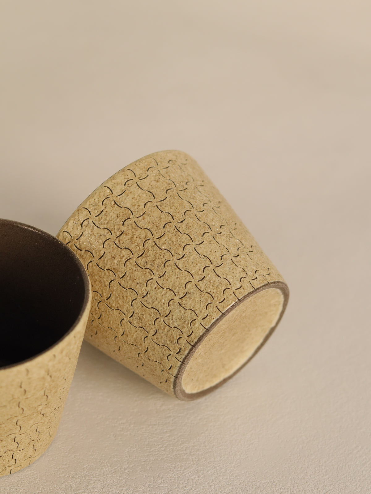 Hand-carved beige ceramic cup resting on its side beside a matching cup.