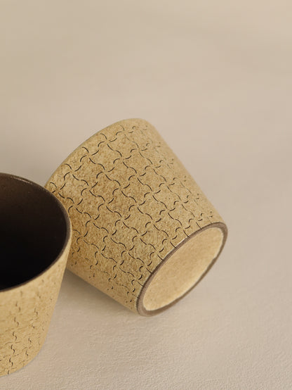Hand-carved beige ceramic cup resting on its side beside a matching cup.