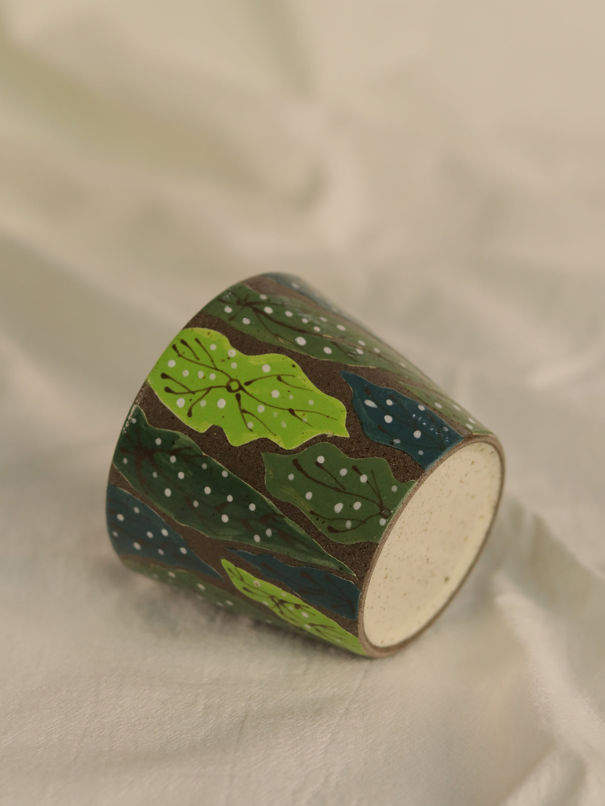 Forest leaf ceramic cup resting on its side, showing the hand-carved botanical pattern.
