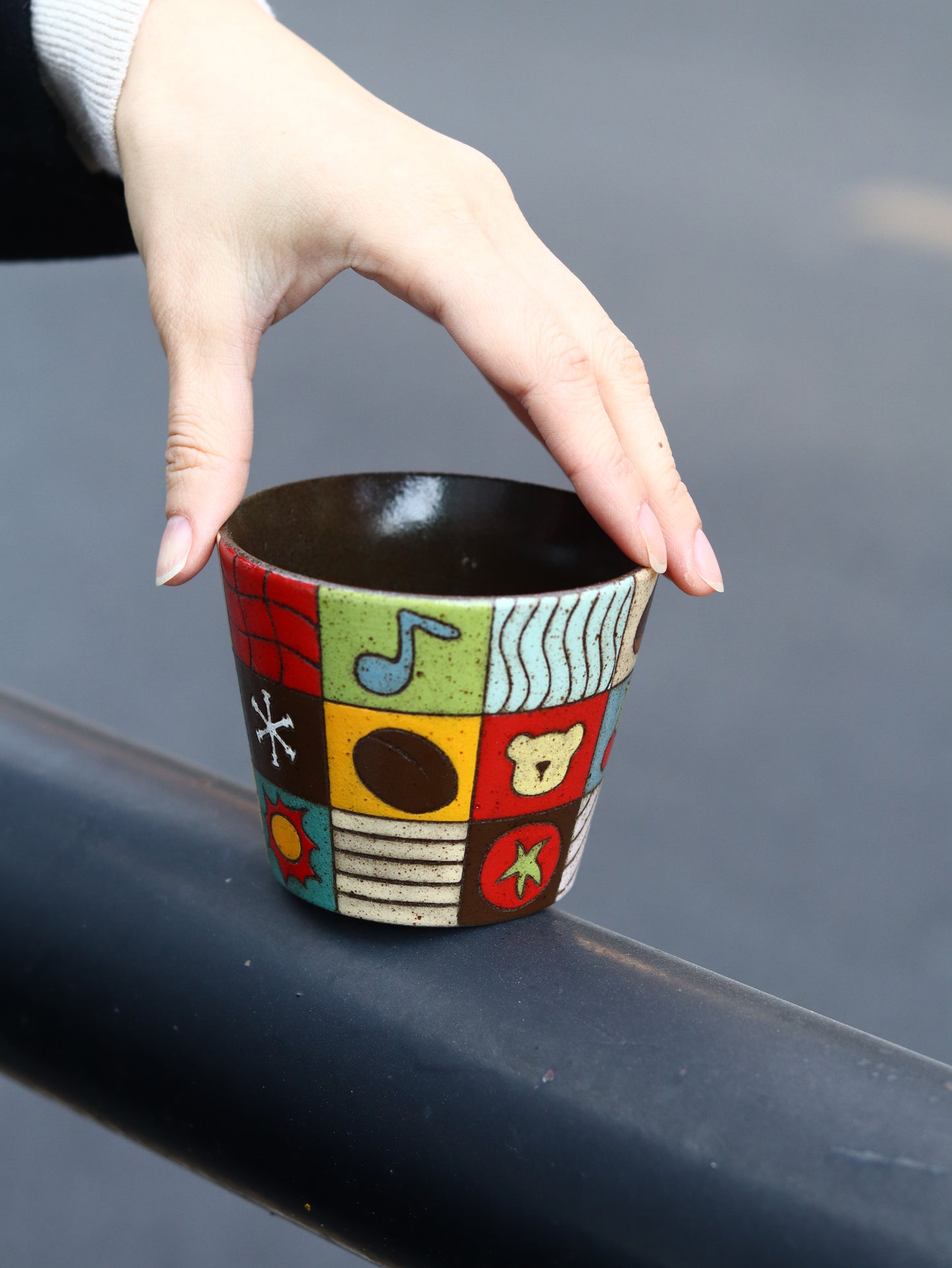 Hand holding a colorful ceramic cup with abstract designs against a gray background