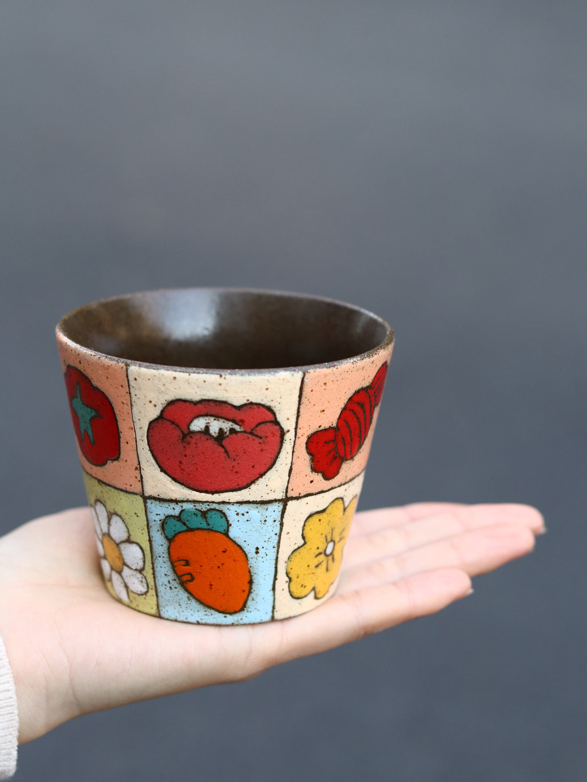 Hand holding a 270ml patchwork cup with a dark glazed interior.