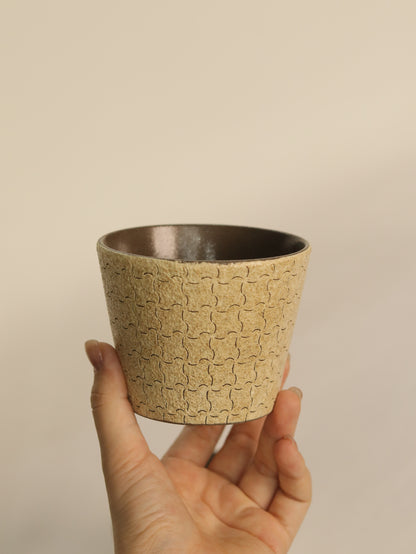 Hand holding a beige ceramic cup decorated with finely carved repeating lines.