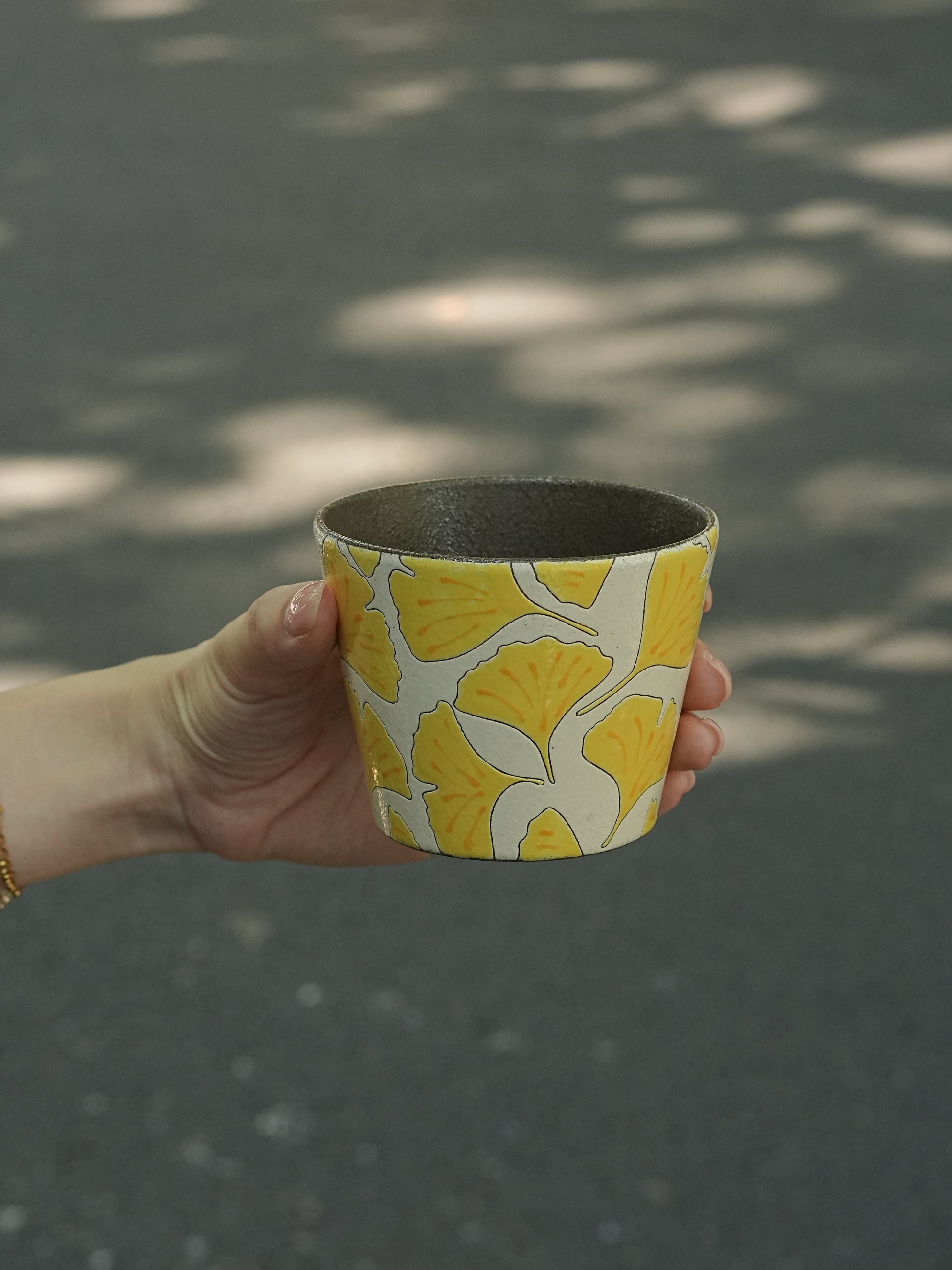 Hand holding a 270ml hand-painted ginkgo ceramic cup with carved yellow leaf outlines