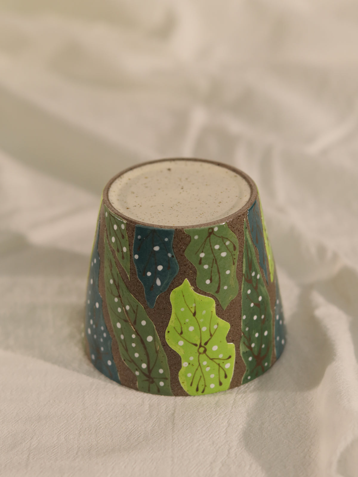 Upside-down forest leaf pottery clay cup showing its base and wraparound green design.