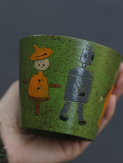 Green ceramic cup with hand-carved scarecrow and tin man illustrations