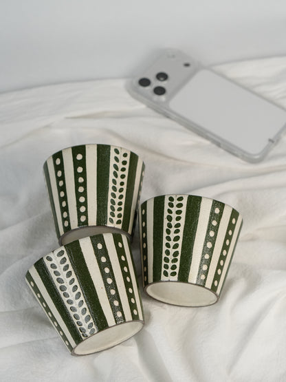 Three green and white patterned cups on a white fabric background with a phone in the background.