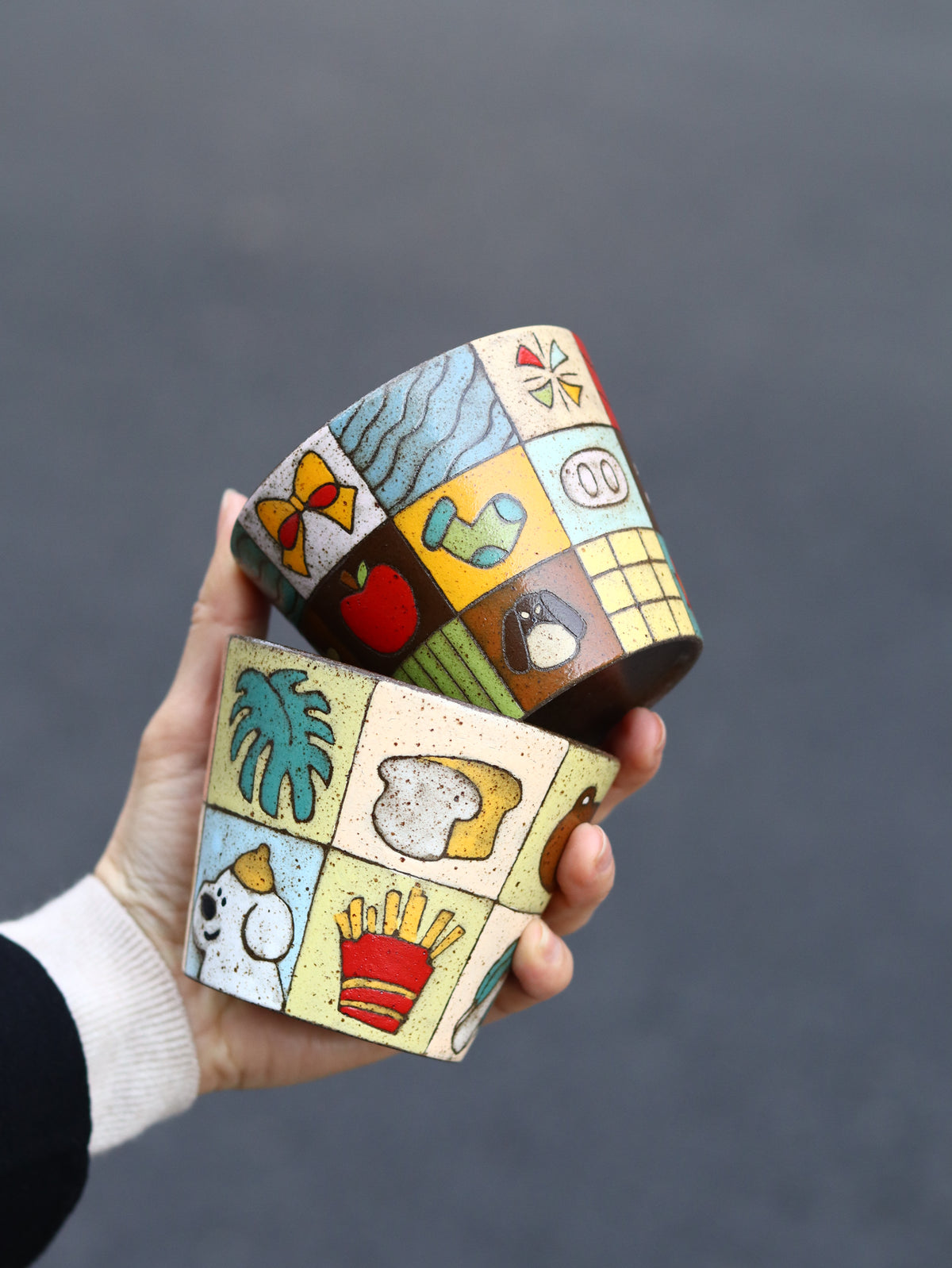 Two colourful patchwork ceramic cups stacked in one hand.
