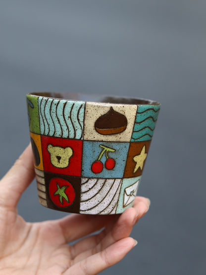 Ceramic cup with colorful patchwork design held by a hand against a gray background