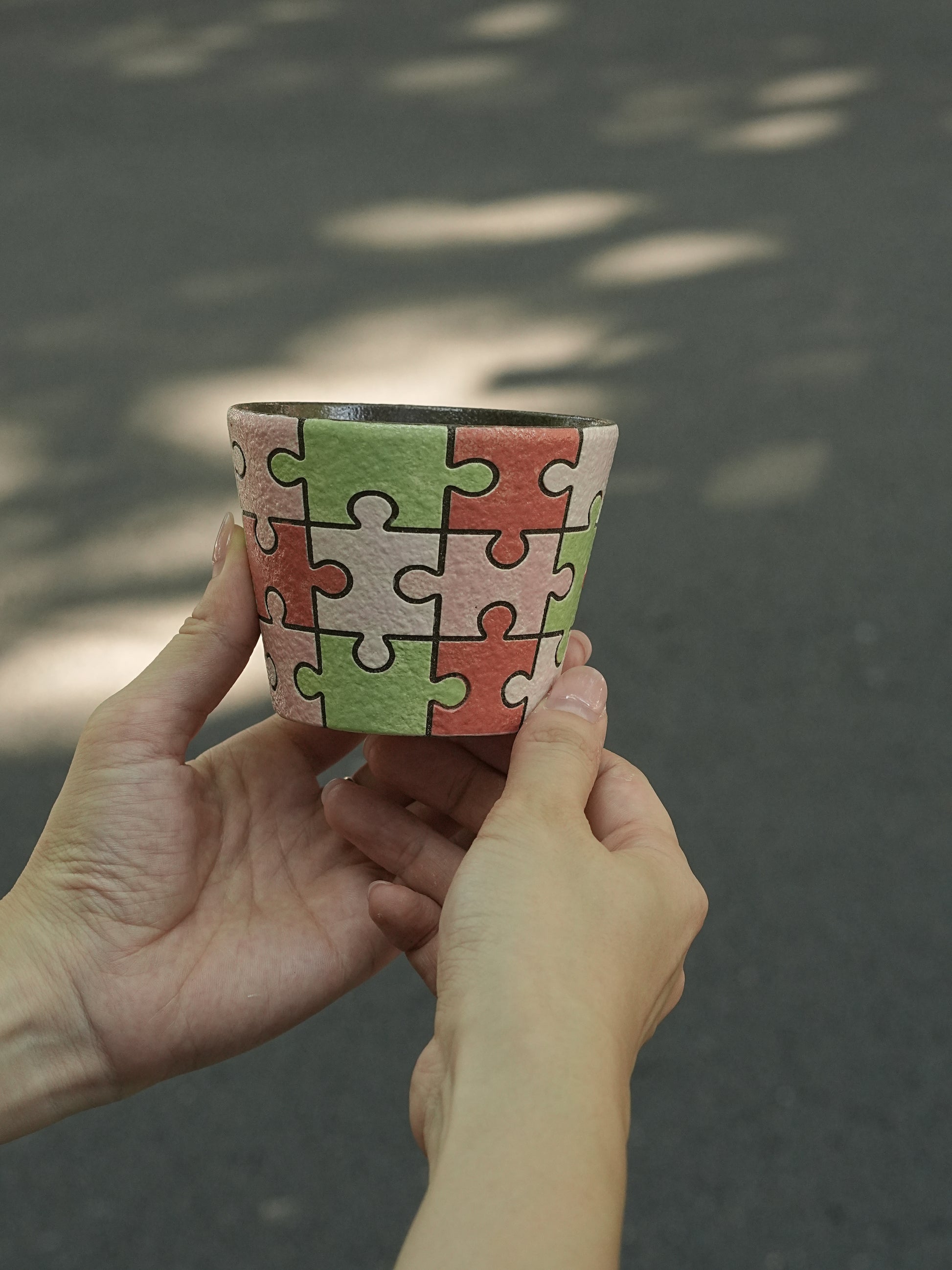 Close-up of a hand-painted puzzle ceramic cup with carved outlines in pink, green and ivory