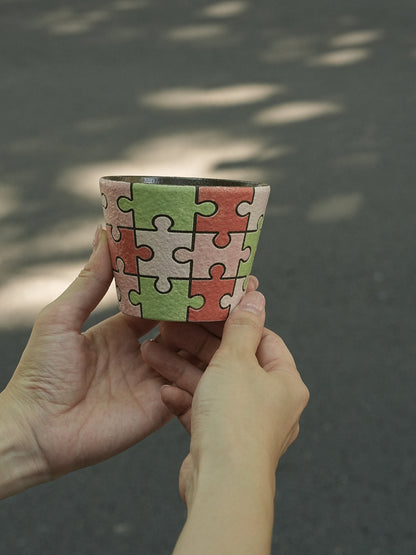 Close-up of a hand-painted puzzle ceramic cup with carved outlines in pink, green and ivory