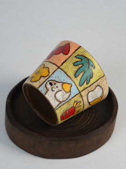 Patchwork ceramic cup resting on its side on a wooden stand.