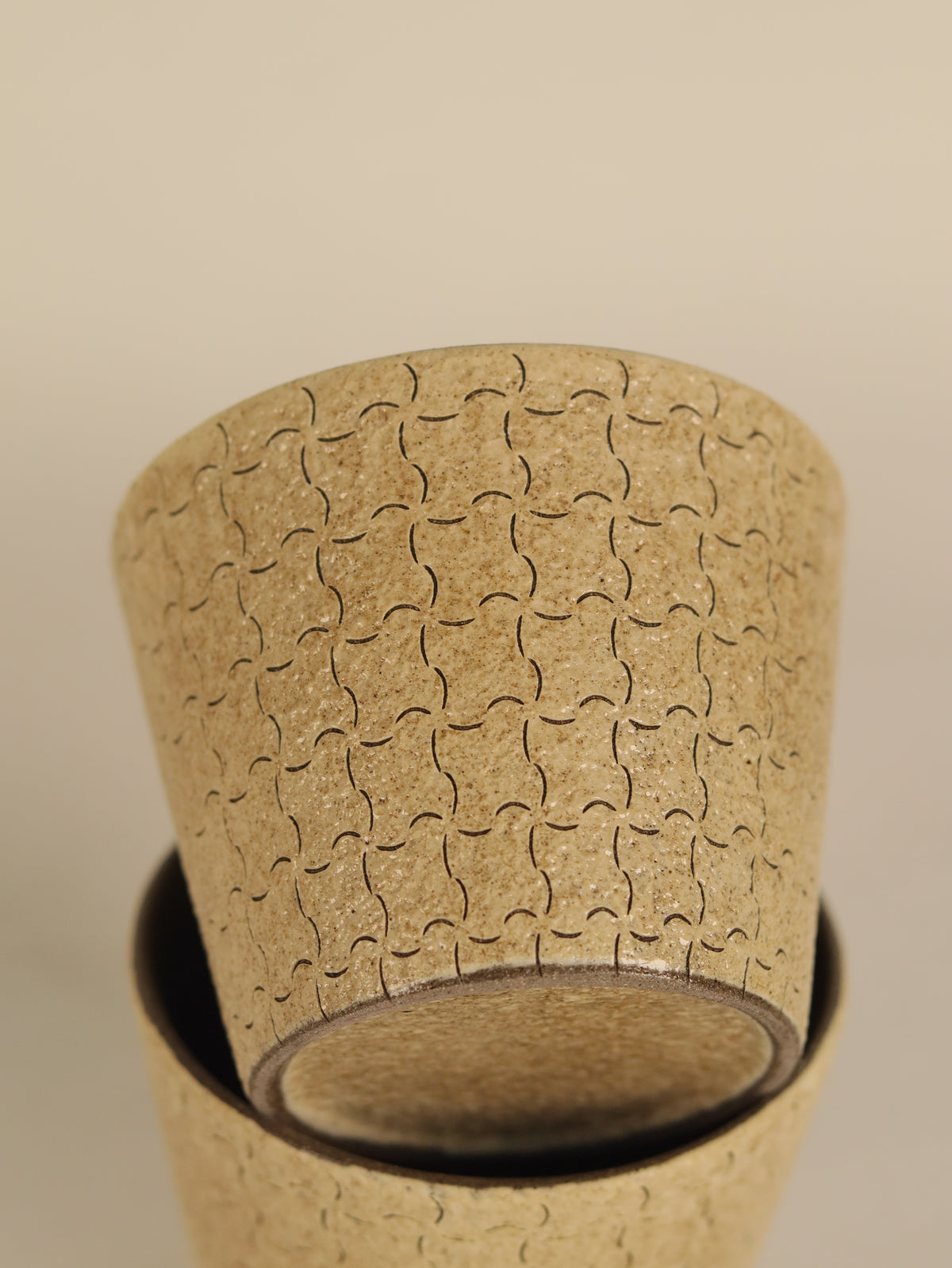 Close-up of a geometric ceramic cup showing its hand-carved pattern and base.