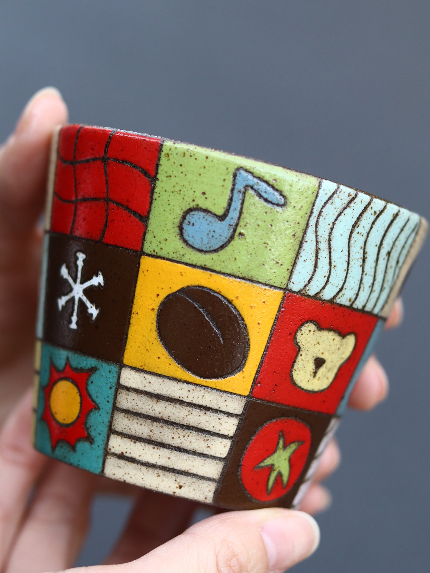 Ceramic mug with colorful geometric design held by a hand against a gray background