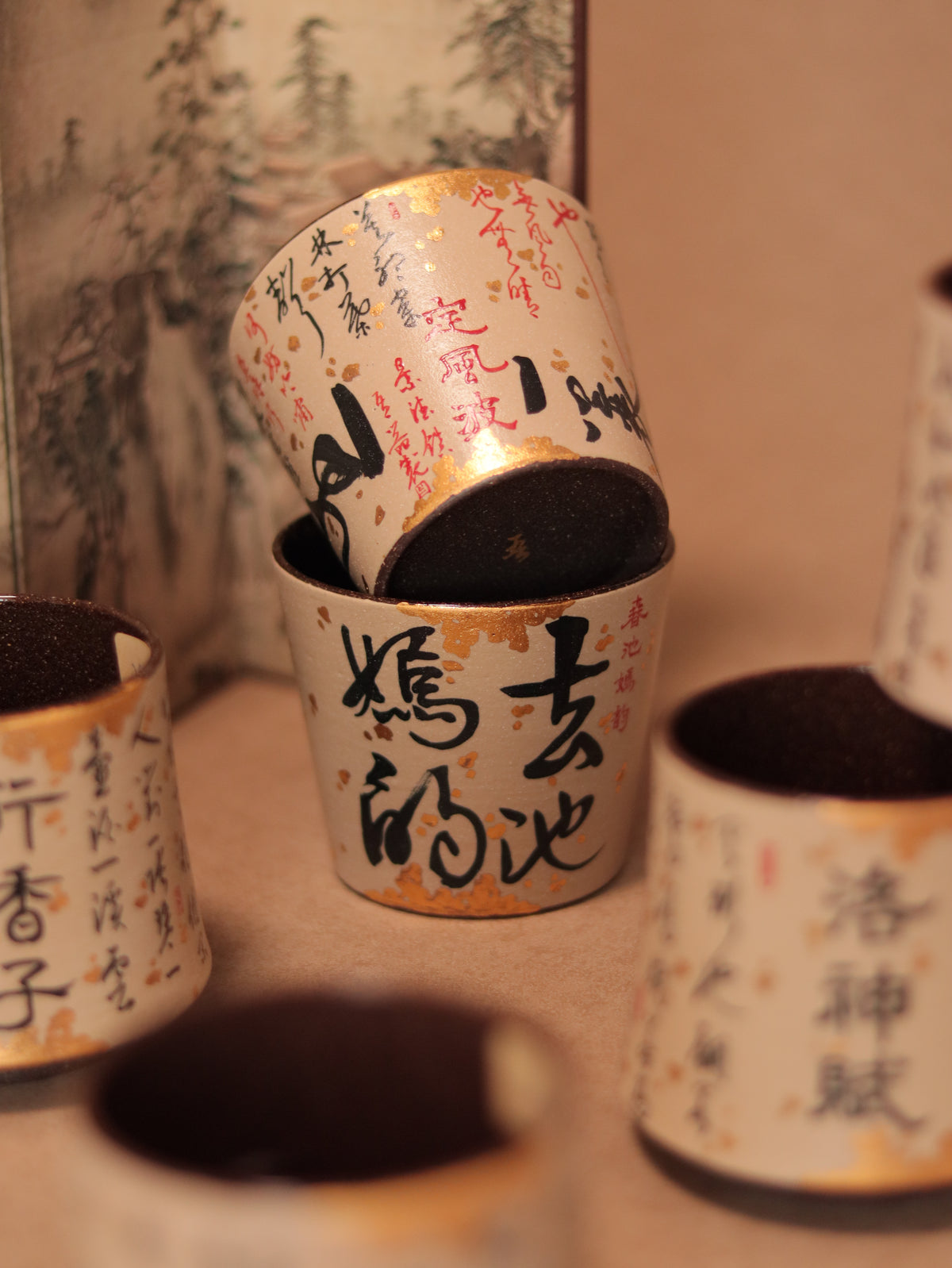 Hand-painted Chinese calligraphy ceramic cups displayed together, showing black characters, red accents and gold-fleck detailing.