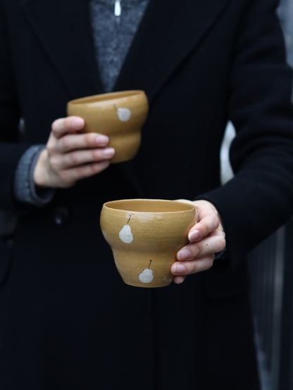 Two hands holding small wooden cups with white spots against a dark background