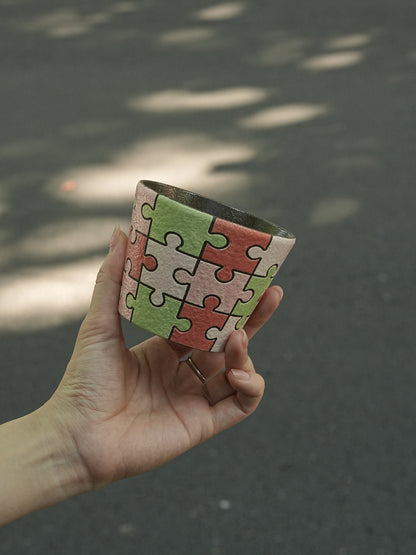Close-up of a hand-painted puzzle ceramic cup with carved outlines in pink, green and ivory