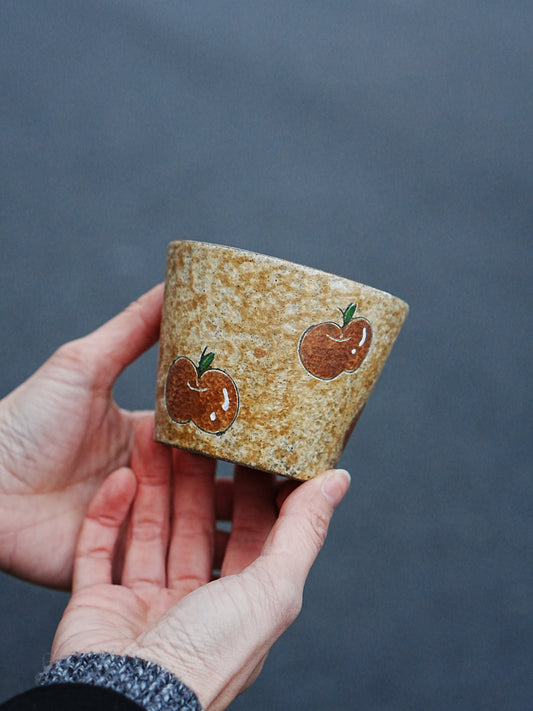 Hand holding a rustic apple ceramic cup with a golden speckled finish and dark glazed interior.