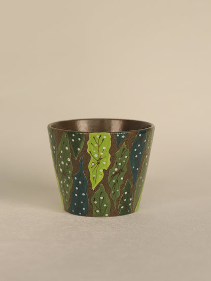 Front view of a hand-carved forest leaf pottery clay cup with layered green botanical details and a dark textured finish.