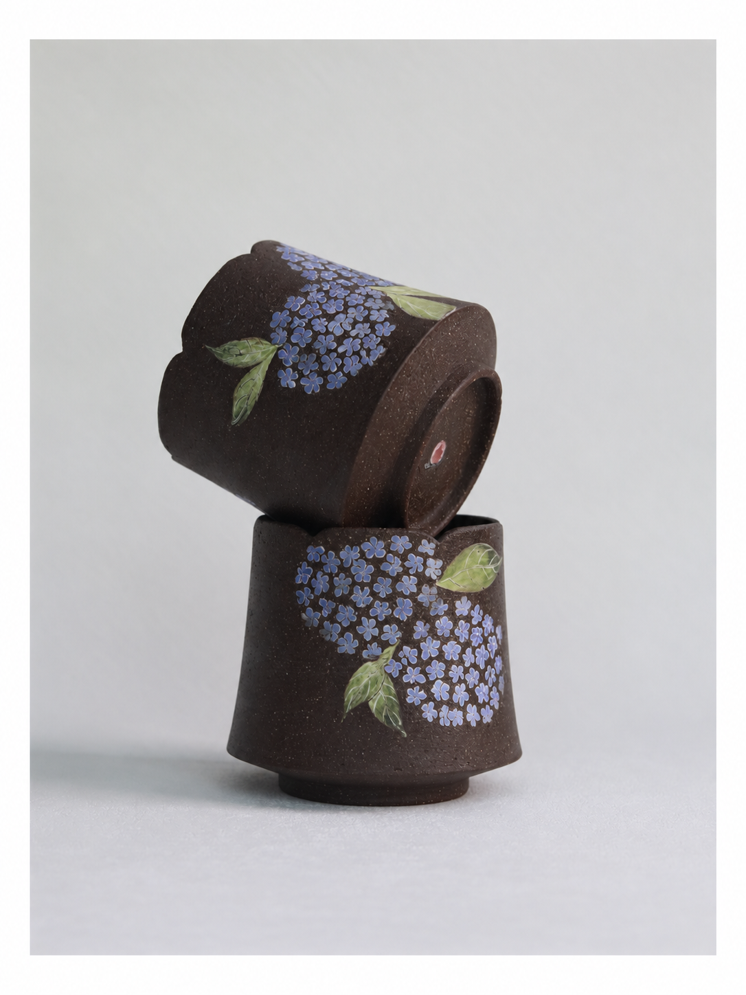 Two dark zisha clay hydrangea cups stacked together, showing their carved floral designs.