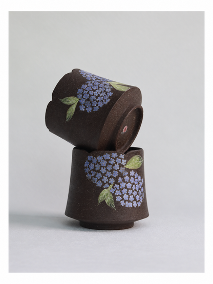 Two dark zisha clay hydrangea cups stacked together, showing their carved floral designs.