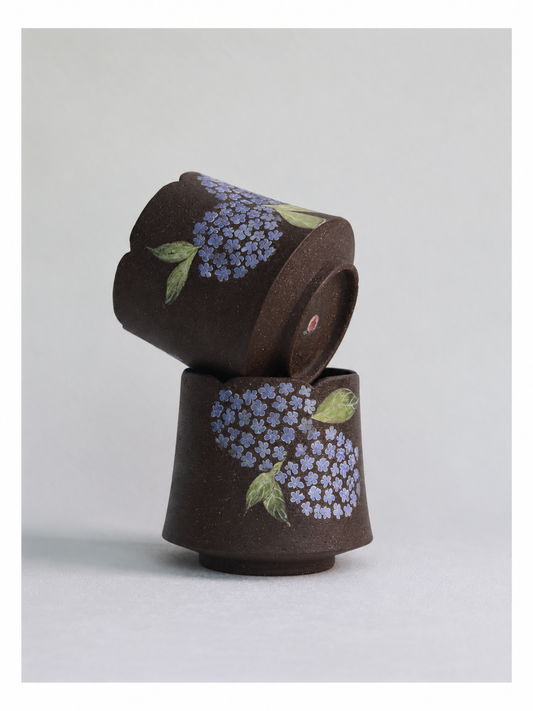 Two dark zisha clay hydrangea cups stacked together, showing their carved floral designs.