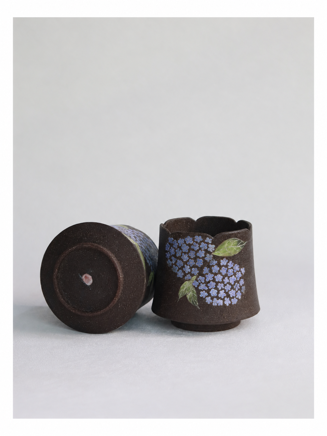 Hand-carved hydrangea cup displayed upright beside a second cup showing its pottery clay base.