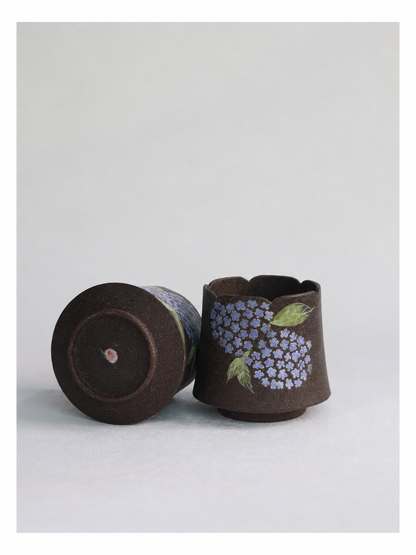 Hand-carved hydrangea cup displayed upright beside a second cup showing its pottery clay base.