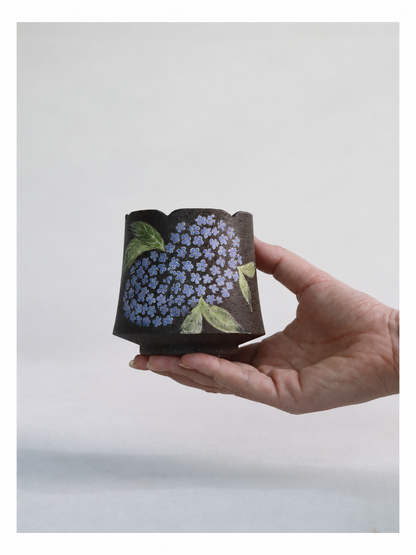 Hand holding a 250ml hydrangea zisha clay cup with a gently scalloped rim.