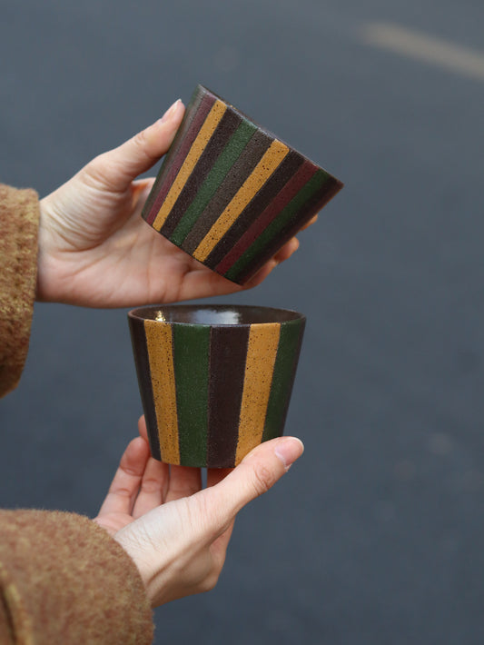 Two hands holding striped cylindrical objects against a dark background