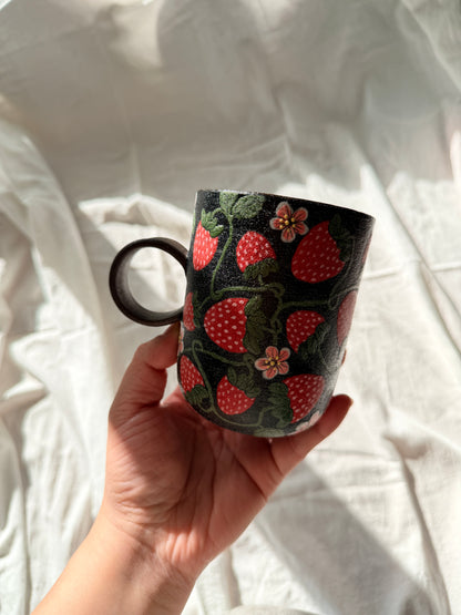Hand holding a mug with strawberry pattern against a white fabric background