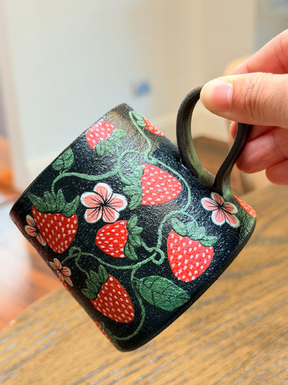 Mug with strawberry and flower pattern held by a hand on a wooden surface
