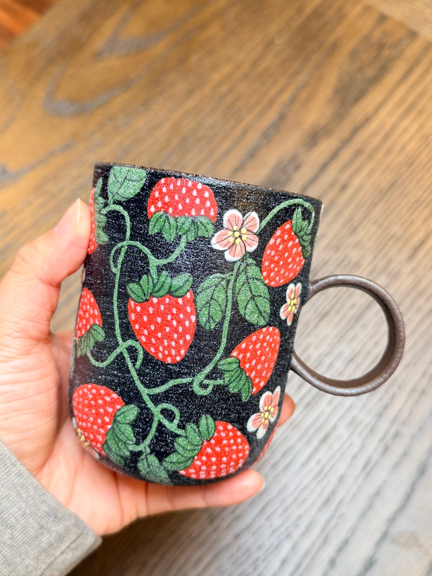 Hand holding a mug with strawberry pattern on a wooden surface