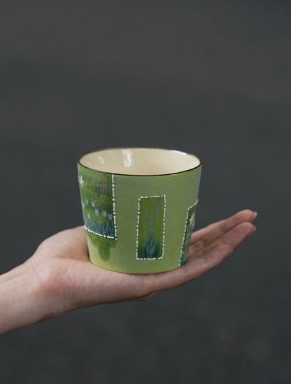 Green ceramic cup showing raised glaze frame and garden artwork