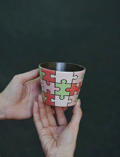 Close-up of a hand-painted puzzle ceramic cup with carved outlines in pink, green and ivory