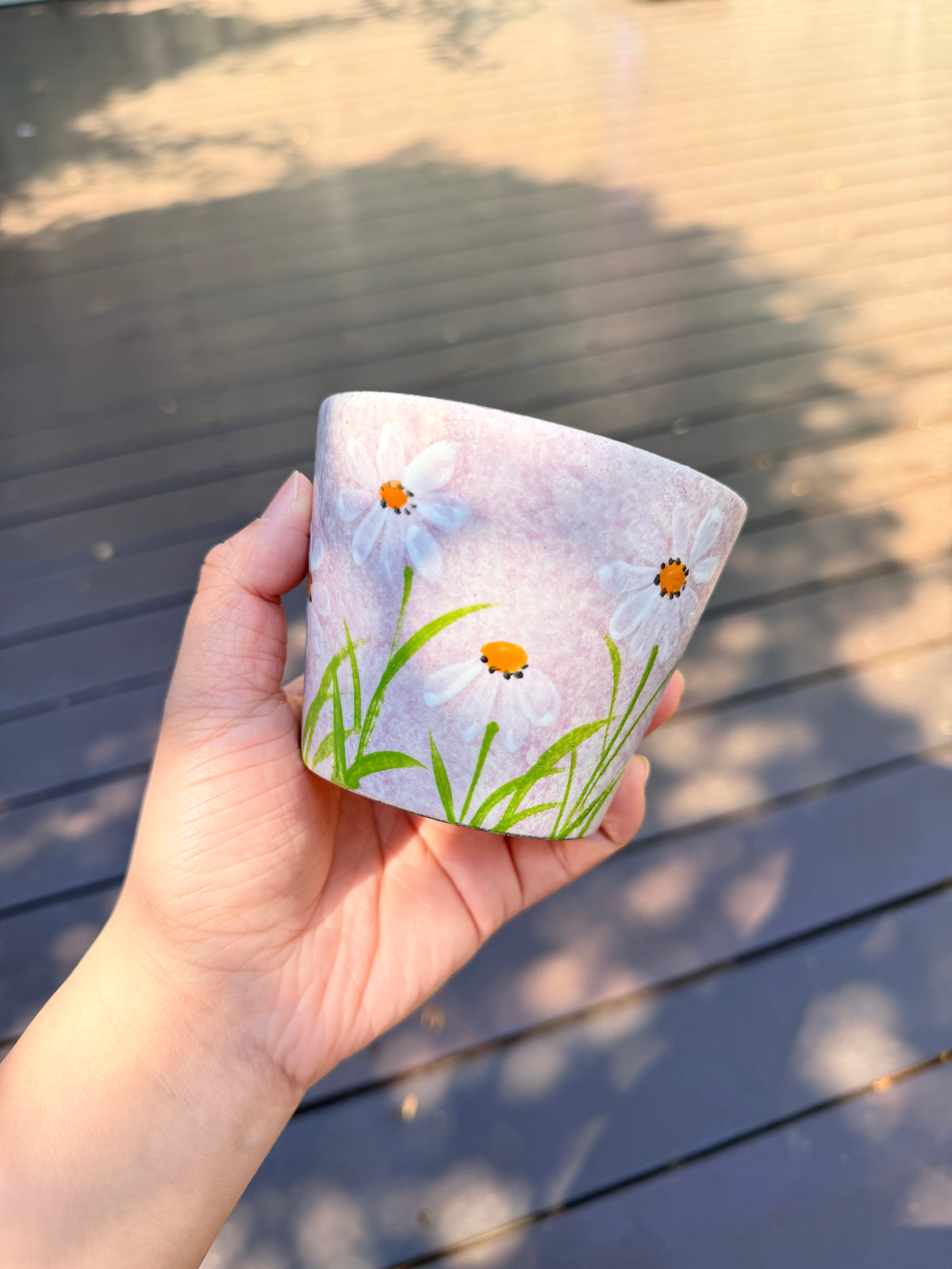Hand holding a 270ml pink ceramic cup with hand-painted white daisies and green leaves